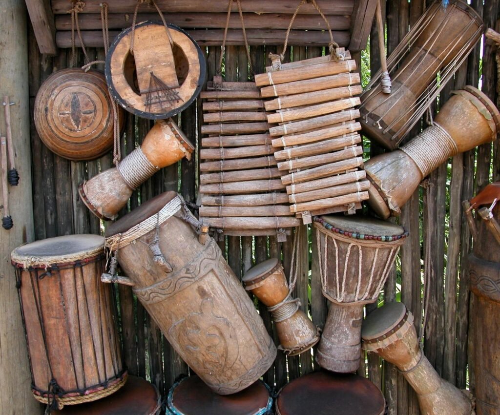 A variety of rustic handmade percussion instruments displayed on a wooden wall.