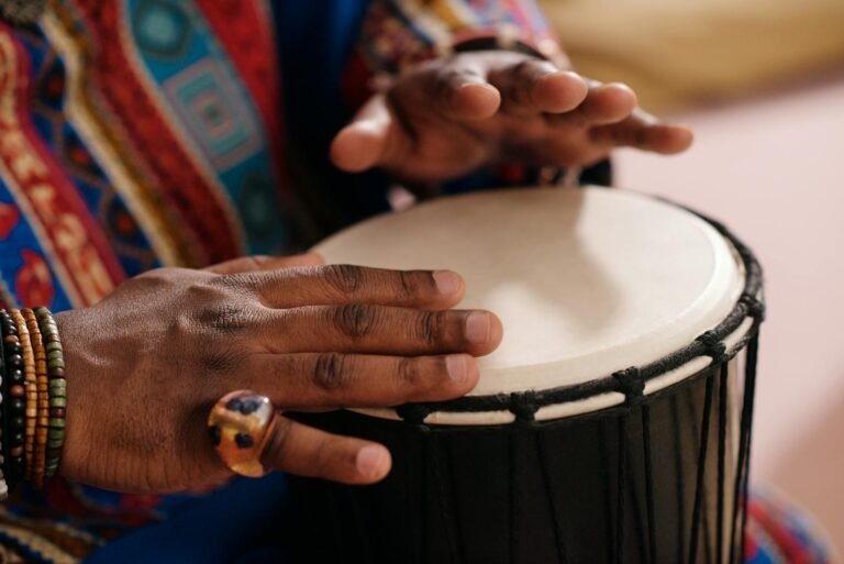 Hands playing a djembe drum, showcasing vibrant cultural clothing and traditional jewelry.