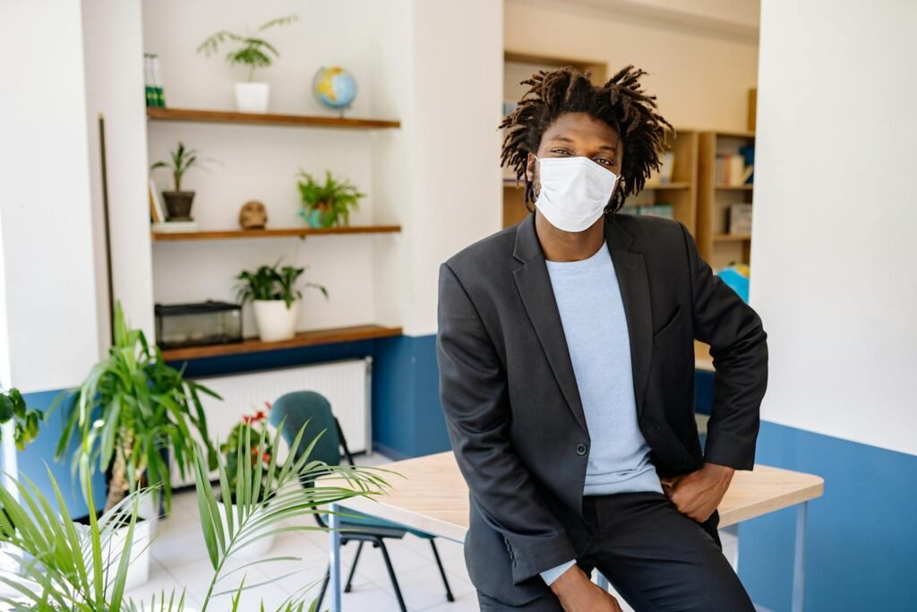 African American man in suit with face mask seated in modern office environment. - pharmacopée africaine
